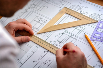 Man architect draws a plan, graph, design, geometric shapes by pencil on large sheet of paper at office desk