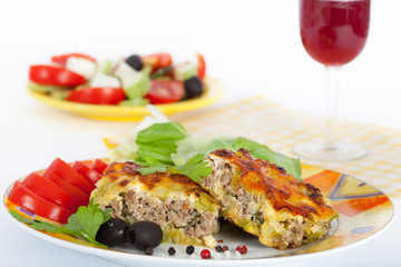 A traditional moussaka, made with layers of minced meat and zucchini,  topped with cheese and bechamel sauce and served with wine and salad.