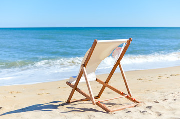 Back View Of Woman's Hat and Deckchair On Sandy Beach