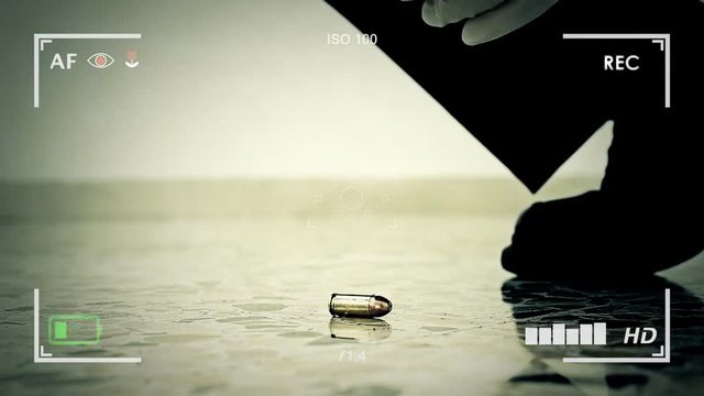 An investigator on a crime scene collecting a bullet from the floor with pliers and storing it in a plastic bag. Seen through the viewfinder of a recording camera.