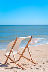 Fototapeta na wymiar Back View Of Woman's Hat and Deckchair On Sandy Beach