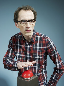 A nerdy guy with his hand poised above a red game show buzzer