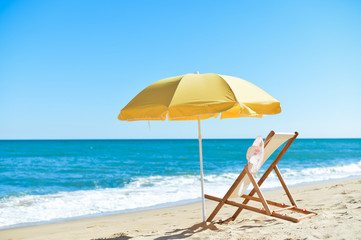 Back View Of Sun Parasol, Woman's Hat and Deckchair On Sandy Beach 