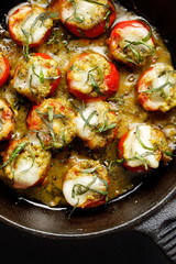  Roasted cherry tomatoes stuffed with herb pesto and mozzarella cheese on a cast-iron frying pan, top view