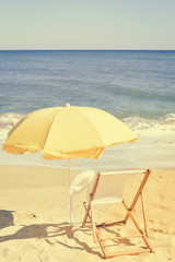 Back View Of Sun Parasol, Woman's Hat and Deckchair On Sandy Beach 