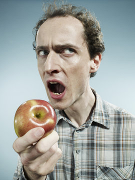 A frowning man preparing to bite into an apple