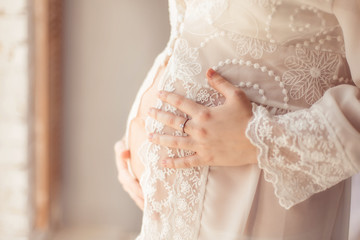 Pregnant woman in gentle white peignoir holding her belly