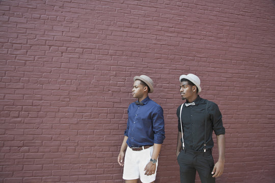 Two handsome young black men walking next to a brick wall