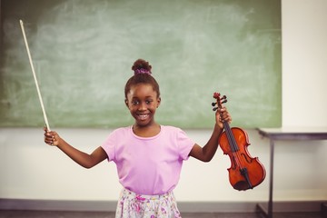 Portrait of smiling schoolgirl holding violin in classroom