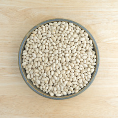 Full bowl of organic navy beans on a wood table top view.