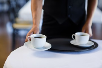 Mid section of waitress serving cup of coffee