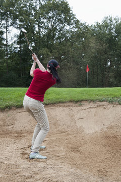 A female golfer hitting a ball out of a sand trap