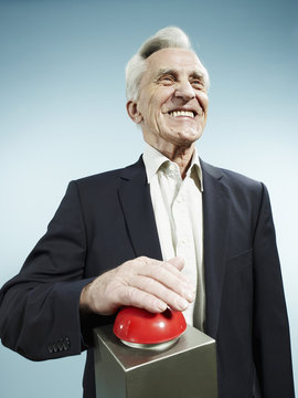 A grinning senior man pushing a red game show buzzer