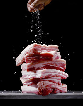 Person sprinkling salt onto pork belly