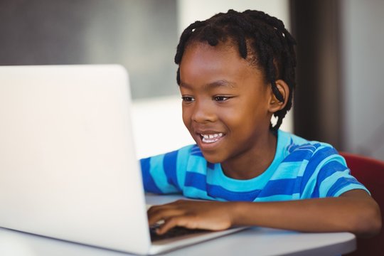 Smiling schoolboy using laptop in classroom