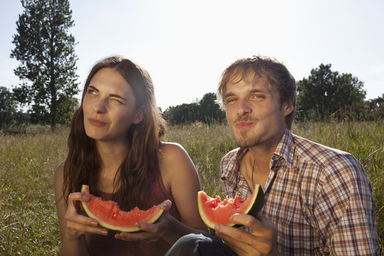 Couple sitting eating melon in field