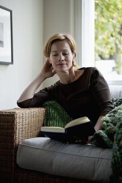 A woman reading a book while reclining on a sofa