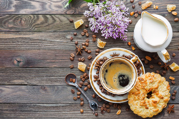 Rustic wooden background with cup of coffee, milk, peanut tart, sugar ginger and lilac flowers....