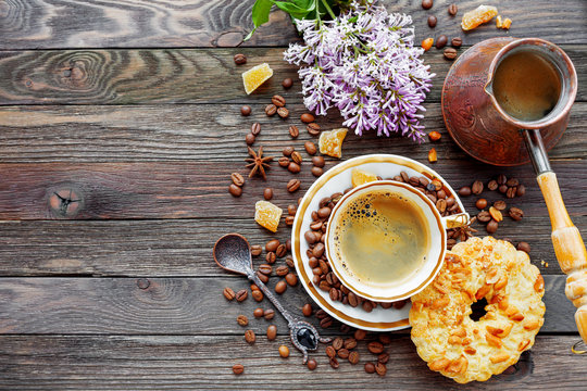 Rustic wooden background with cup and cezve of coffee, peanut tart and lilac flowers.  Breakfast at summer morning. Top view, place for text.