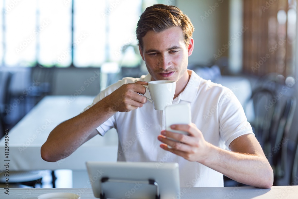 Poster man using mobile phone while having cup of coffee