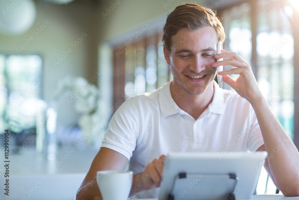 Poster Smiling man talking on mobile phone while using digital tablet