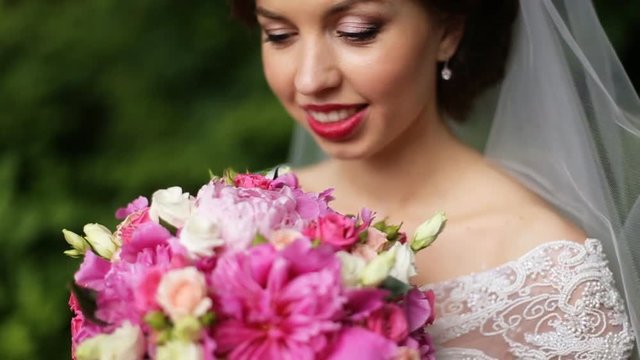A portrait of gentle, sensual and very beautiful bride in a white dress and veil, natural makeup, with a bouquet of pink flowers, close-up