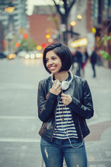 Portrait of beautiful Hispanic latin girl woman short black hair in leather jacket with headphones outside in evening night city street smiling laughing looking away, lifestyle portrait concept