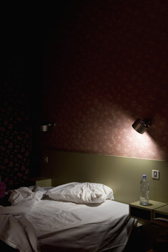 An unmade bed illuminated by a lamp at night