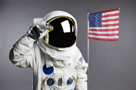 An astronaut saluting next to an American flag, studio shot