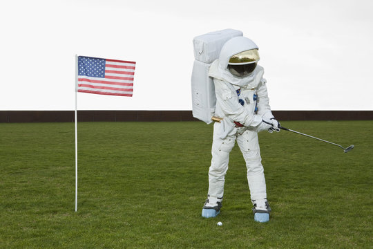 An astronaut swinging a golf club next to an American flag