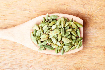 Green cardamom pods on wooden spoon