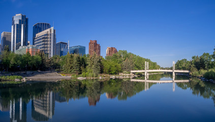Fototapeta na wymiar Foot bridge reflected in the Bow River at princes island park and the urban skyline in Calgary Alberta.