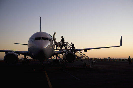 People Boarding An Airplane At Dusk