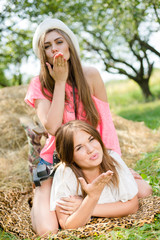 portrait of blowing kiss 2 pretty girls best friends having fun relaxing lying on hay happy smiling & looking at camera on green summer outdoors copy space background