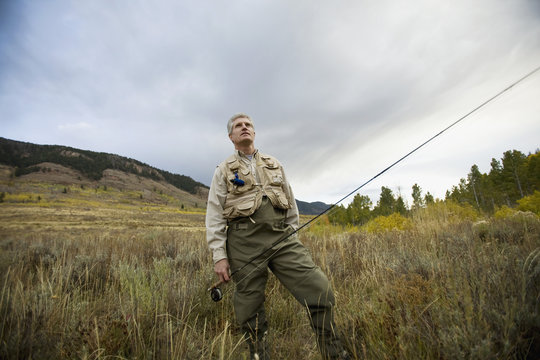 A man standing in a field with a fly rod 