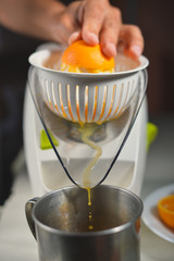 Hand making orange juice with juicer on kitchen table background. Closeup