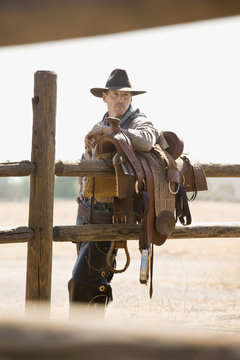 A rancher leaning against a saddle on a fence