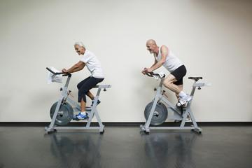 A senior woman and a mature man riding stationary bikes