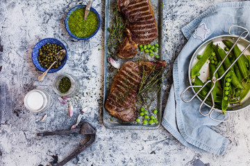 BBQ pork steak with pesto sauce,pea pod, capers and green vegetables over stone table.