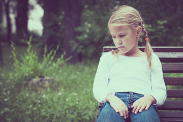 Portrait of sad blond little girl sitting on bench