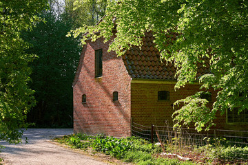 Old barn house of red bricks, with small iron windows, lying in the outskirts of a danish forest, paths of gravel are leading by