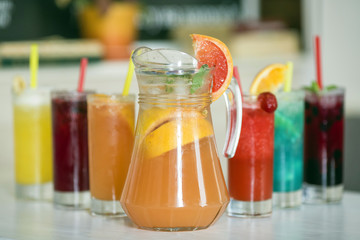 Grapefruit lemonade in jag and colorful beverages in glass on wood background