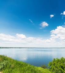 deep blue sky with clouds over river and green grass