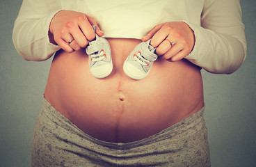 Small shoes for the unborn baby on the belly of pregnant woman