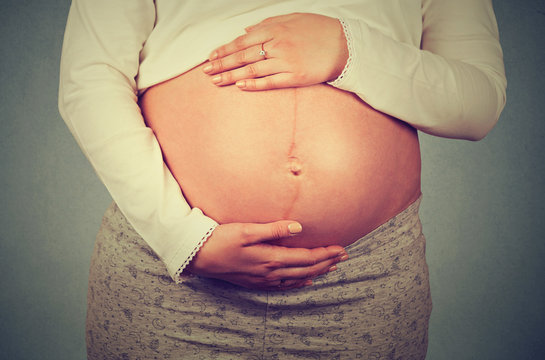 Side profile close up of a cute pregnant belly isolated on gray wall background with copy space