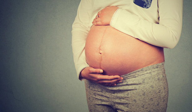 Side profile close up of a cute pregnant belly isolated on gray wall background with copy space