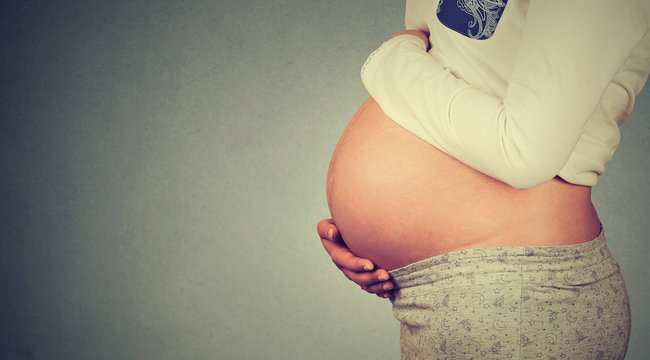 Side profile close up of a cute pregnant belly isolated on gray wall background with copy space