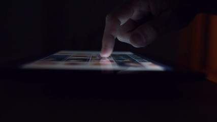 Man browsing online photography portfolio using digital tablet computer, male hand in dark room tapping on touch screen