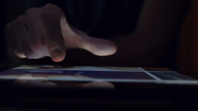 Man browsing online photography portfolio using digital tablet computer, male hand in dark room tapping on touch screen