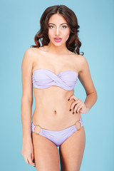 Obraz premium Young sexy woman in purple swimsuit over blue background